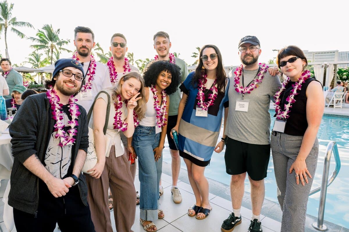Image 2: Group of nine colleagues smiling together by a hotel pool, wearing floral leis at an outdoor company event in Hawaii.