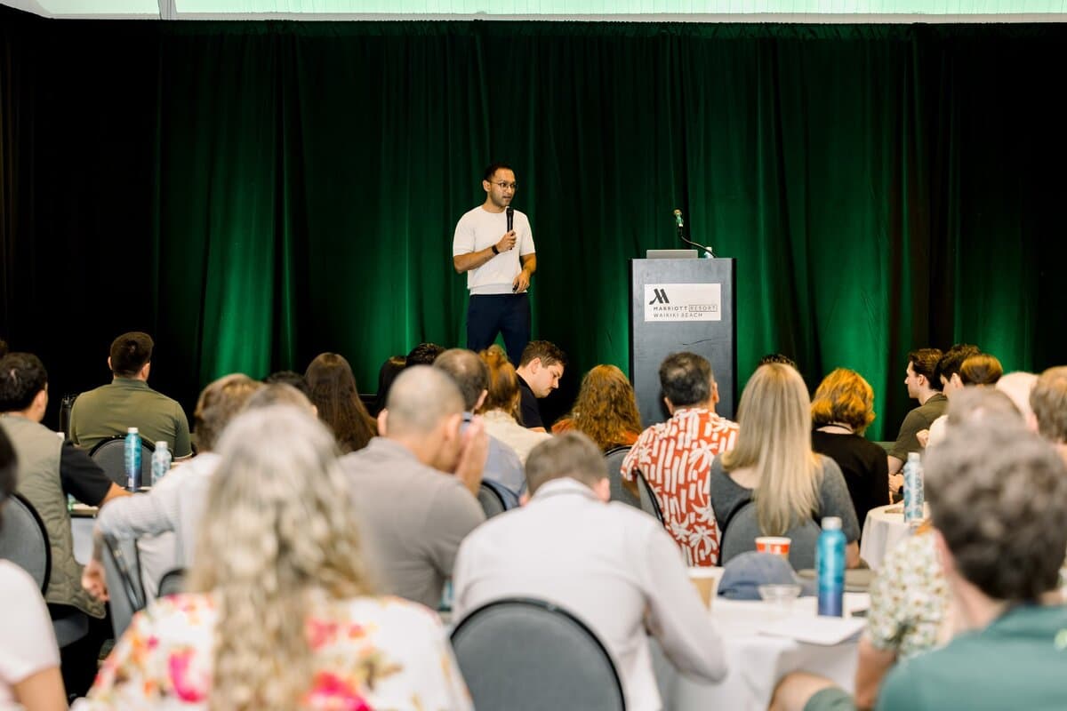 Image 4: A speaker addresses a full conference room from a stage at the Marriott Resort Waikiki Beach during a company all-hands session.